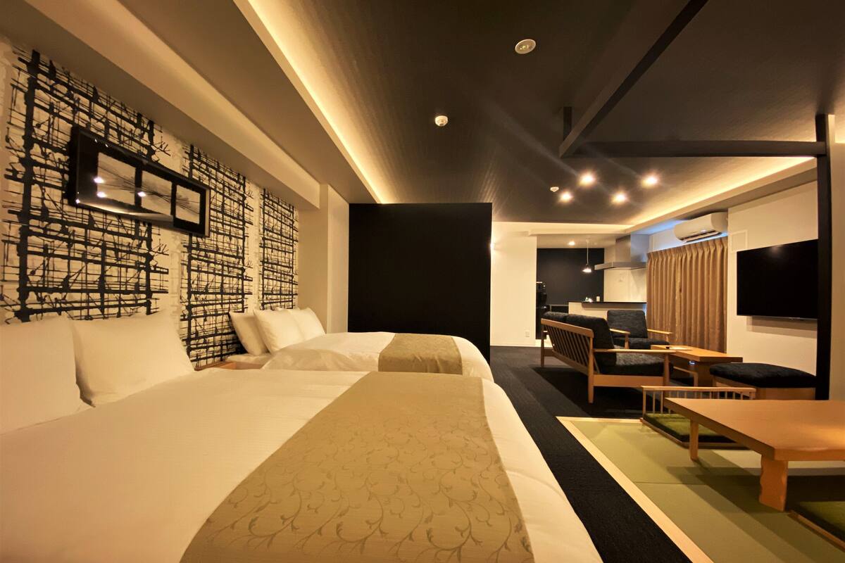 A modern hotel room with a large bed, a desk, a chair, a TV, and a wall with abstract art.