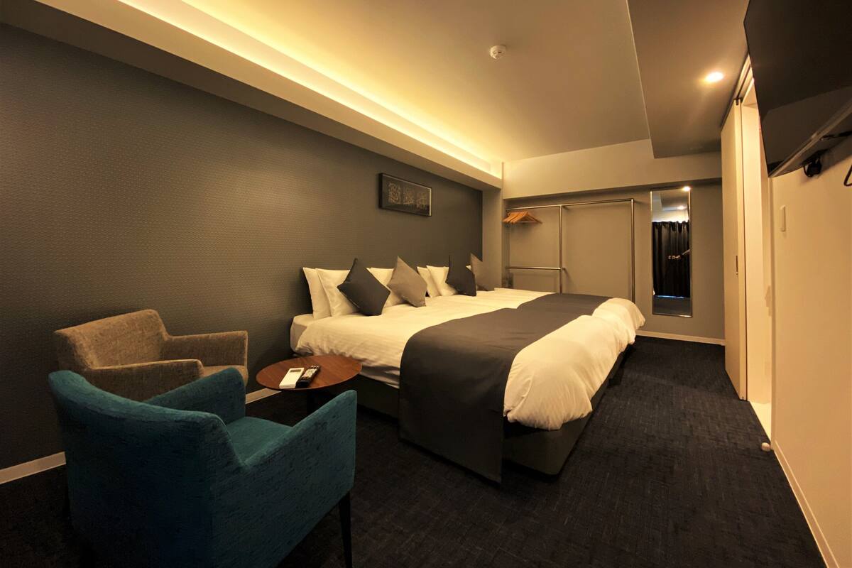 A hotel room with a bed, a chair, a bedside table, and a wardrobe.