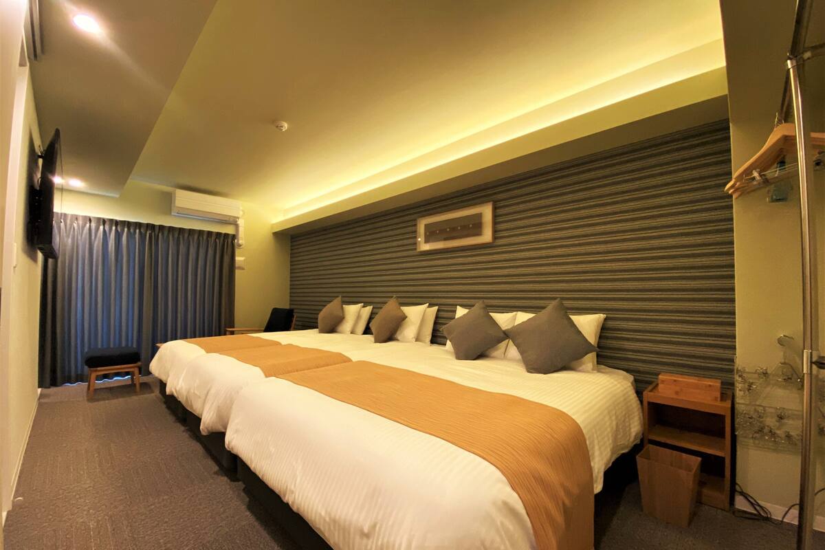 A hotel room with a large bed, a wooden headboard, a small bedside table, a mirror, and a TV mounted on the wall.