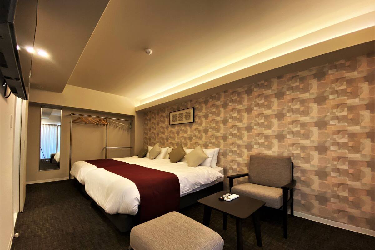 A hotel room with a bed, a chair, a small table, a mirror, and a wardrobe.