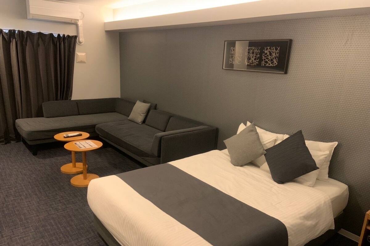 A hotel room with a bed, a sofa, two small tables, and a wall-mounted artwork.