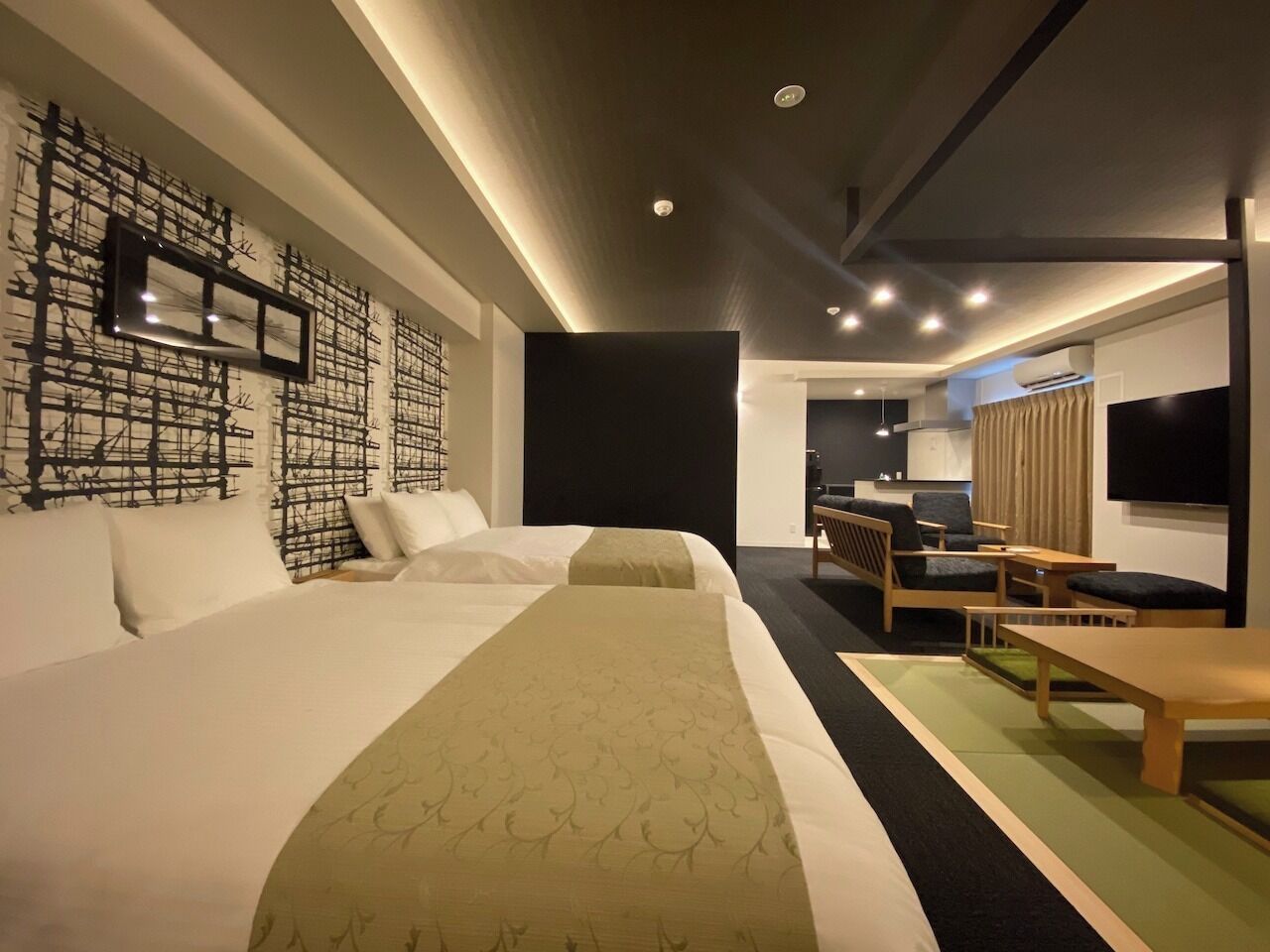 Quarto de hotel com uma cama grande, área de estar com mesa e televisão.