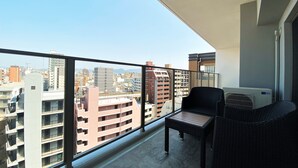 A balcony with wicker furniture, a view of the cityscape, and a white air conditioning unit. - Randor Residential Hotel Fukuoka Annex (Fukuoka)