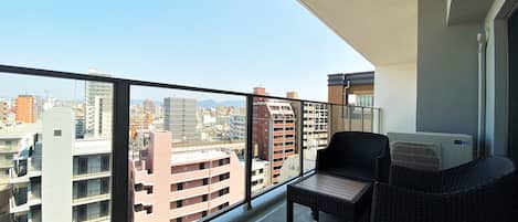 A balcony with wicker furniture, a view of the cityscape, and a white air conditioning unit.