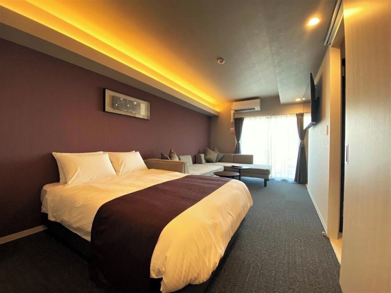 Quarto de hotel com uma cama grande, um sofá, uma mesinha e uma televisão.