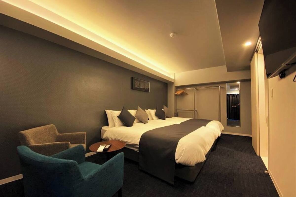 A hotel room with a bed, a chair, a small table, and a wardrobe.