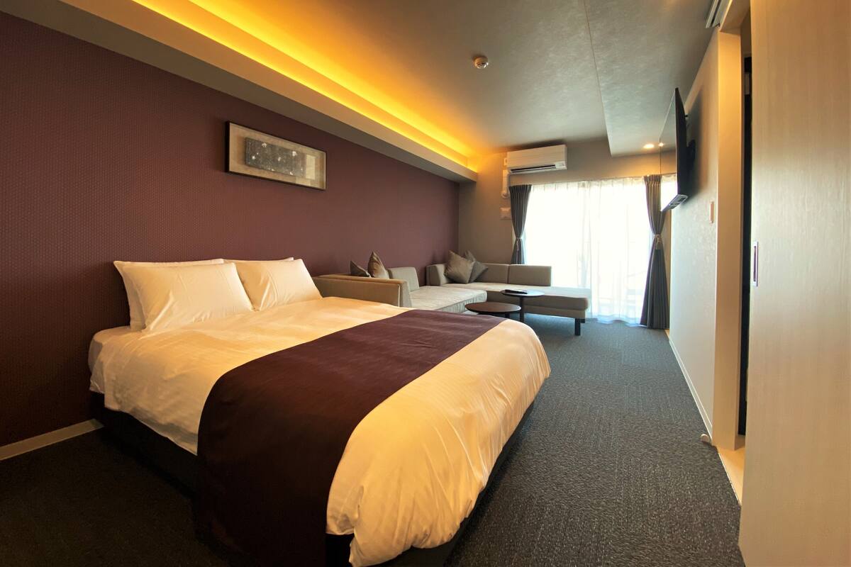 A hotel room with a large bed, a sofa, a small table, and a TV.