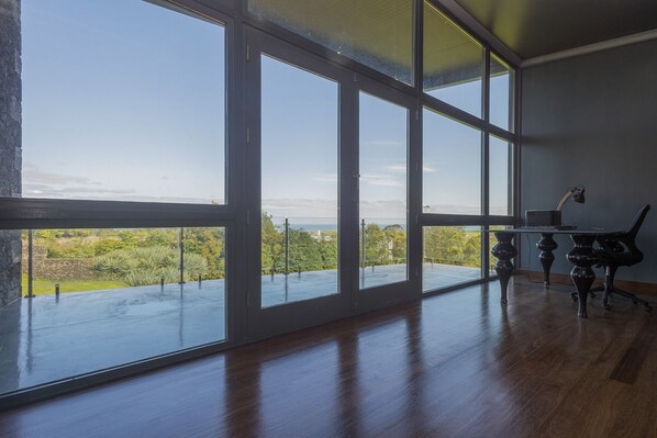 A room with large windows, a wooden floor, and a desk with a chair. - Villa with modern minimalist architecture in the middle of a nature reserve (Rabo de Peixe, Sao Miguel Island, Azores)