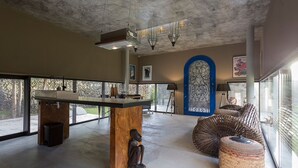 A spacious room with a large window, a central island with a sculpture, a woven bench, and a blue decorative panel.
