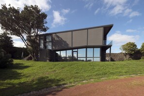 A modern two-story house with a sloped roof, large windows, and a covered outdoor area.