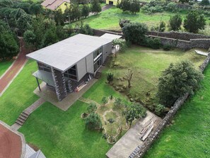 A modern two-story building with a flat roof, surrounded by a well-maintained lawn and a stone wall.