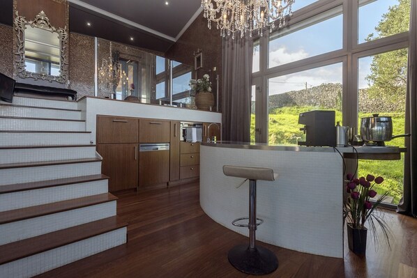 A modern kitchen with a curved island, wooden cabinetry, and a large window offering a view of greenery.