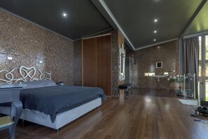 A modern bedroom with a large bed, a wooden wardrobe, a small bench, and a bathroom with a sink and shower.