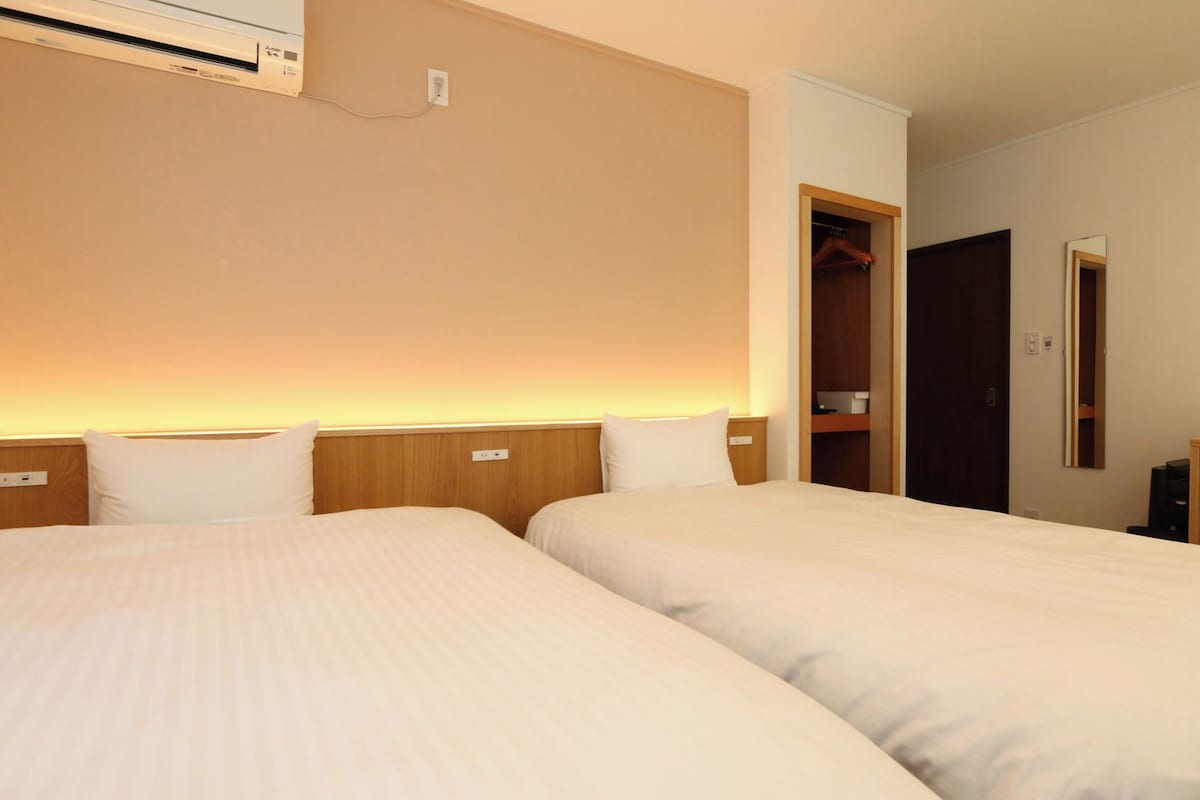 Habitación de hotel con dos camas, un escritorio, una silla y un armario.