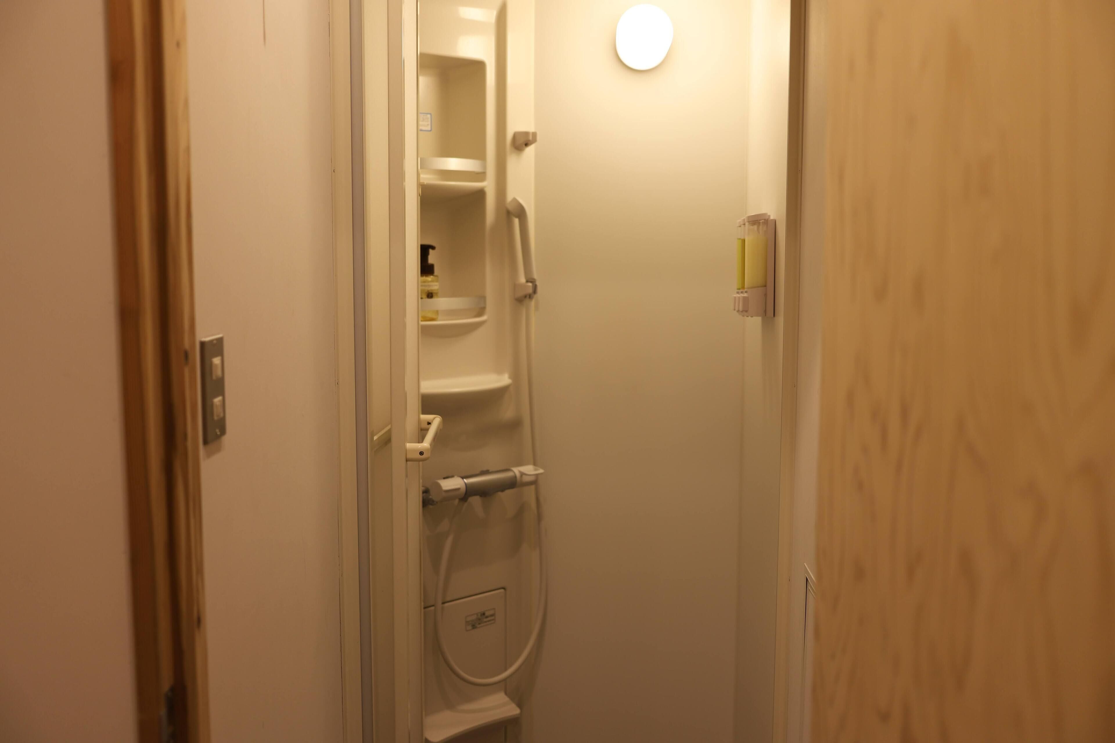 A narrow bathroom with a shower, a toilet, and a small shelf with toiletries.