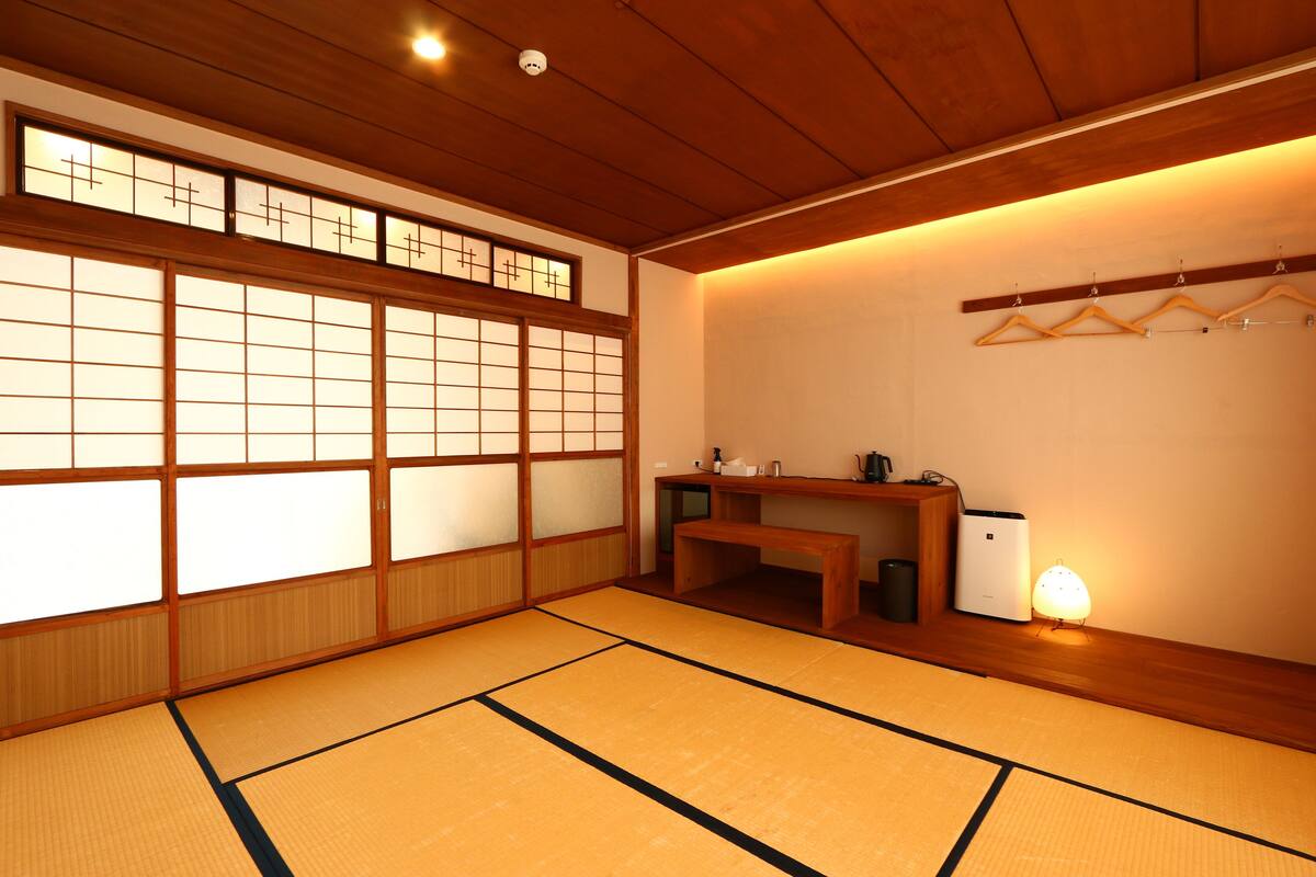 A traditional Japanese room with tatami flooring, shoji screens, a wooden desk, and a hanging clothes rack.