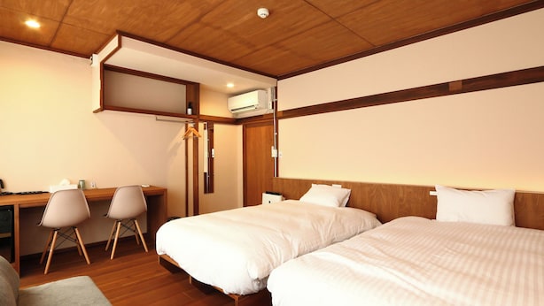 A hotel room with two beds, a desk, chairs, and an air conditioning unit. - nirasakiyaSTAY (Nirasaki)