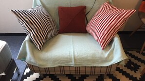 A light green armchair with a plaid skirt, adorned with three pillows in black and white houndstooth, red, and red and white houndstooth patterns. - FC House Shibuya 202 (Tokyo)