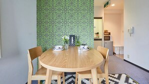 A dining area with a round wooden table, four chairs, and a patterned green wall. - FC House Shibuya 202 (Tokyo)