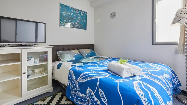 A bedroom with a bed, a TV, a cabinet, a painting, and a window. - FC House Shibuya 202 (Tokyo)
