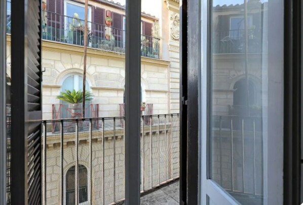 A view from a balcony with a metal railing, looking out onto a building with a stone facade and arched windows.