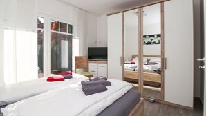 A modern hotel room with a large bed, a TV, a wooden wardrobe, and a window with a view of trees. - Vacation breathing space in Greetsiel (Greetsiel)