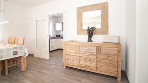 A modern kitchen with white cabinets, a wooden dining table, and a wooden dresser with drawers. - Vacation breathing space in Greetsiel (Greetsiel)