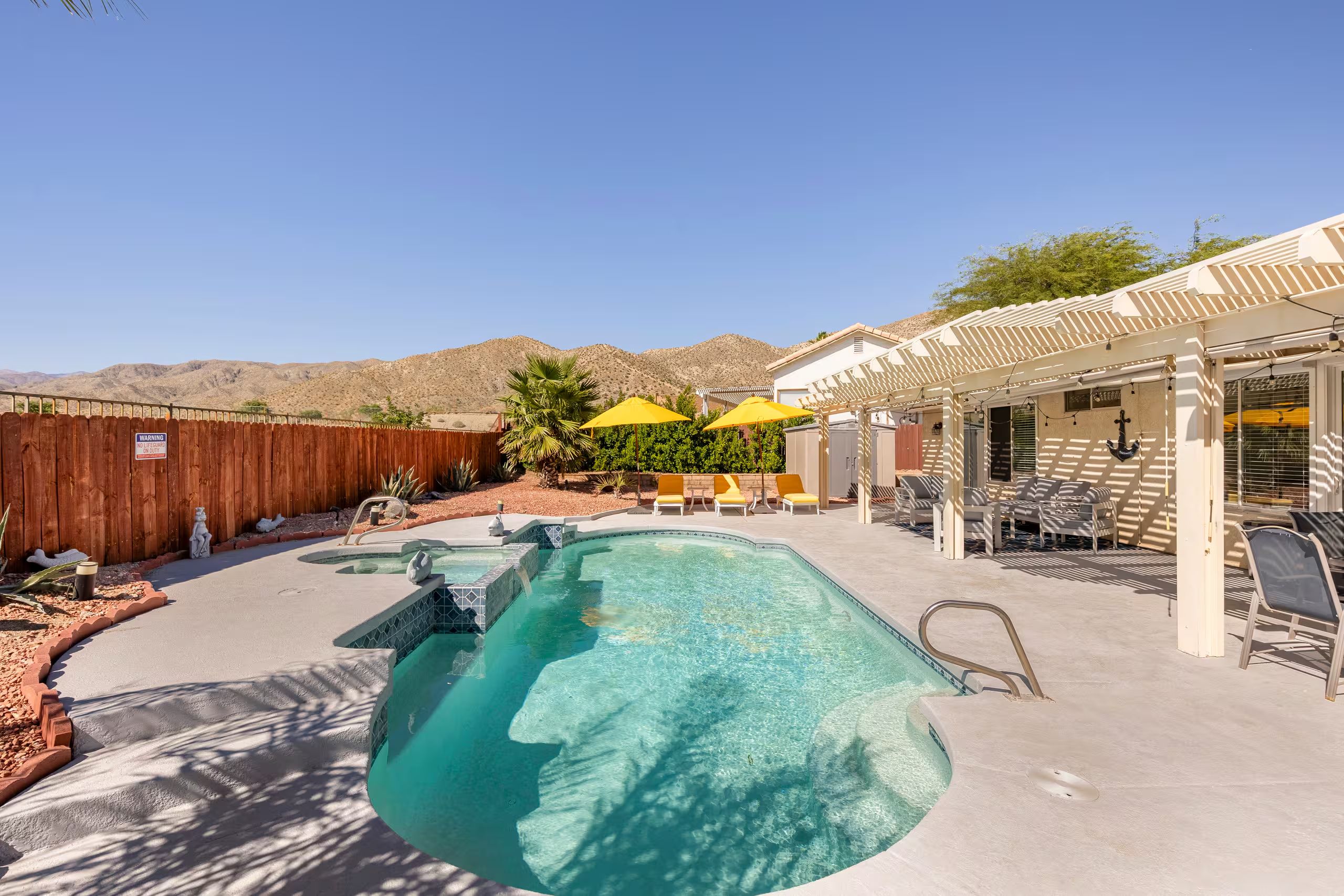 A swimming pool with a wooden fence, outdoor seating, and a mountain backdrop.