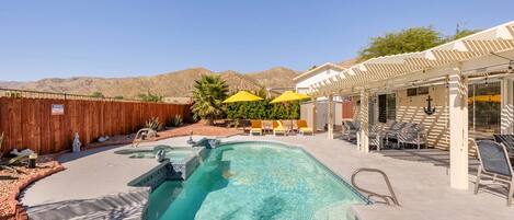 A swimming pool with a wooden fence, outdoor seating, and a mountain backdrop.