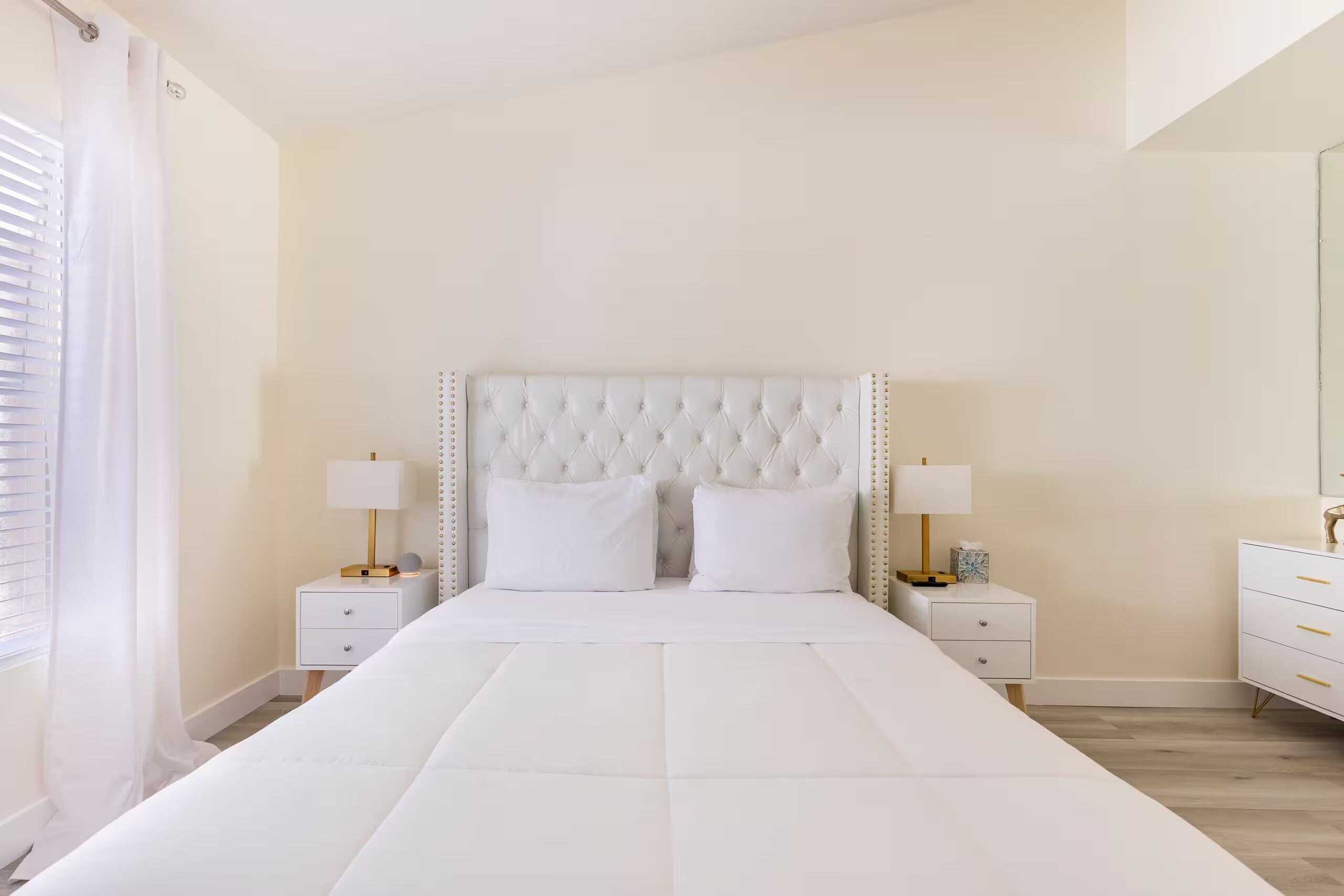 A bedroom with a large bed, two bedside tables with lamps, a dresser, and a mirror.
