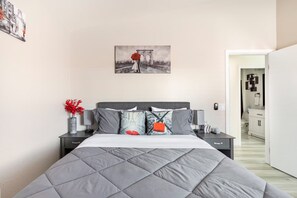 Une chambre à coucher avec un lit, des tables de chevet, un vase rempli de fleurs rouges et un tableau représentant un pont.