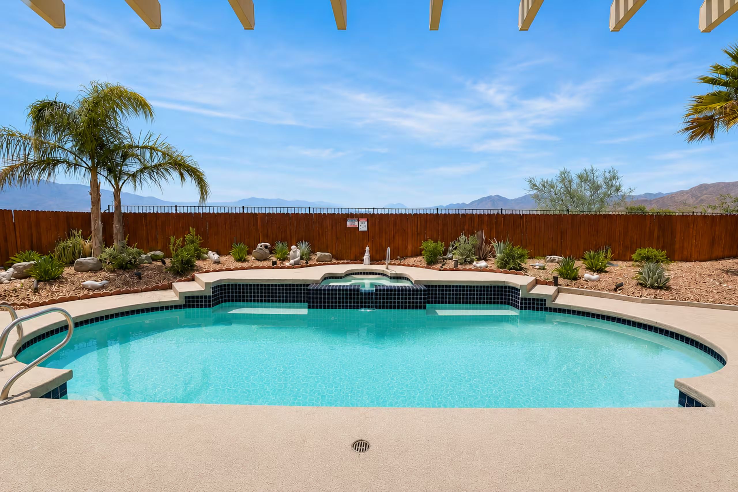 Una piscina con recinzione in legno, palme e piante tipiche del deserto.