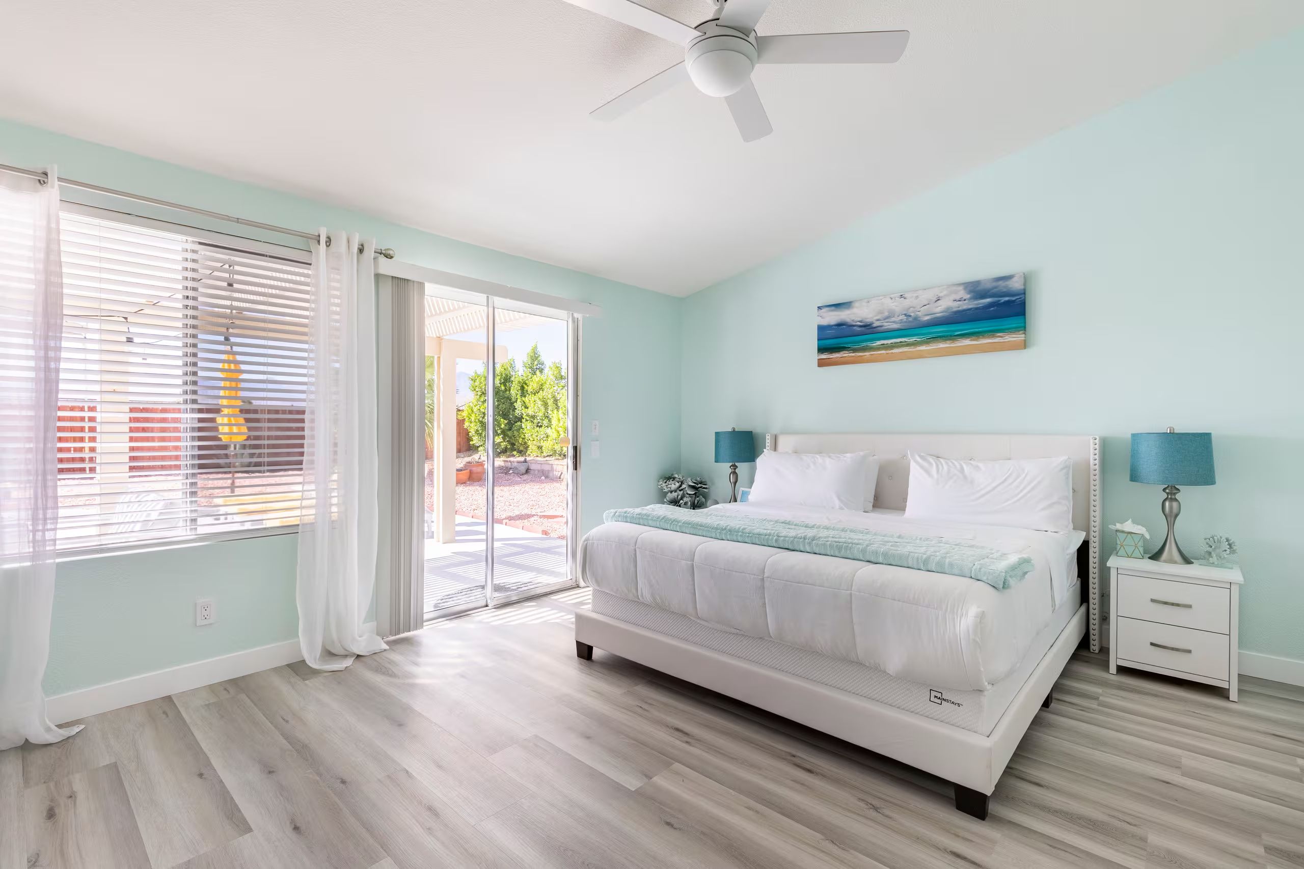 A bedroom with a bed, a nightstand, a ceiling fan, and a view through a sliding glass door.