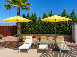A patio area with four white lounge chairs, each with a yellow cushion, under two yellow umbrellas. - Salt Water Pool & Spa with Mountain Sunset Views! (Desert Hot Springs)