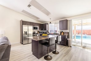 Una cocina moderna con una isla central, muebles oscuros, electrodomésticos de acero inoxidable y vistas a un patio trasero con piscina.