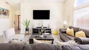 Ein modernes Wohnzimmer mit Flachbildfernseher, einer Couch, einem Couchtisch und Zierpflanzen.