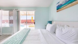 Ein Schlafzimmer mit Bett, einem Gemälde und Blick auf einen Außenbereich mit Pool und Holzzaun.