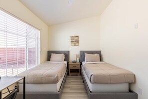 Un dormitorio con dos camas, una mesita de noche, una lámpara de pared y una ventana con persianas.