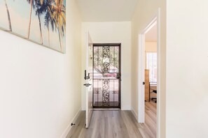 A hallway with a door featuring a decorative metal gate, a painting on the wall, and a view into a room with a desk and chair. - Salt Water Pool & Spa with Mountain Sunset Views! (Desert Hot Springs)