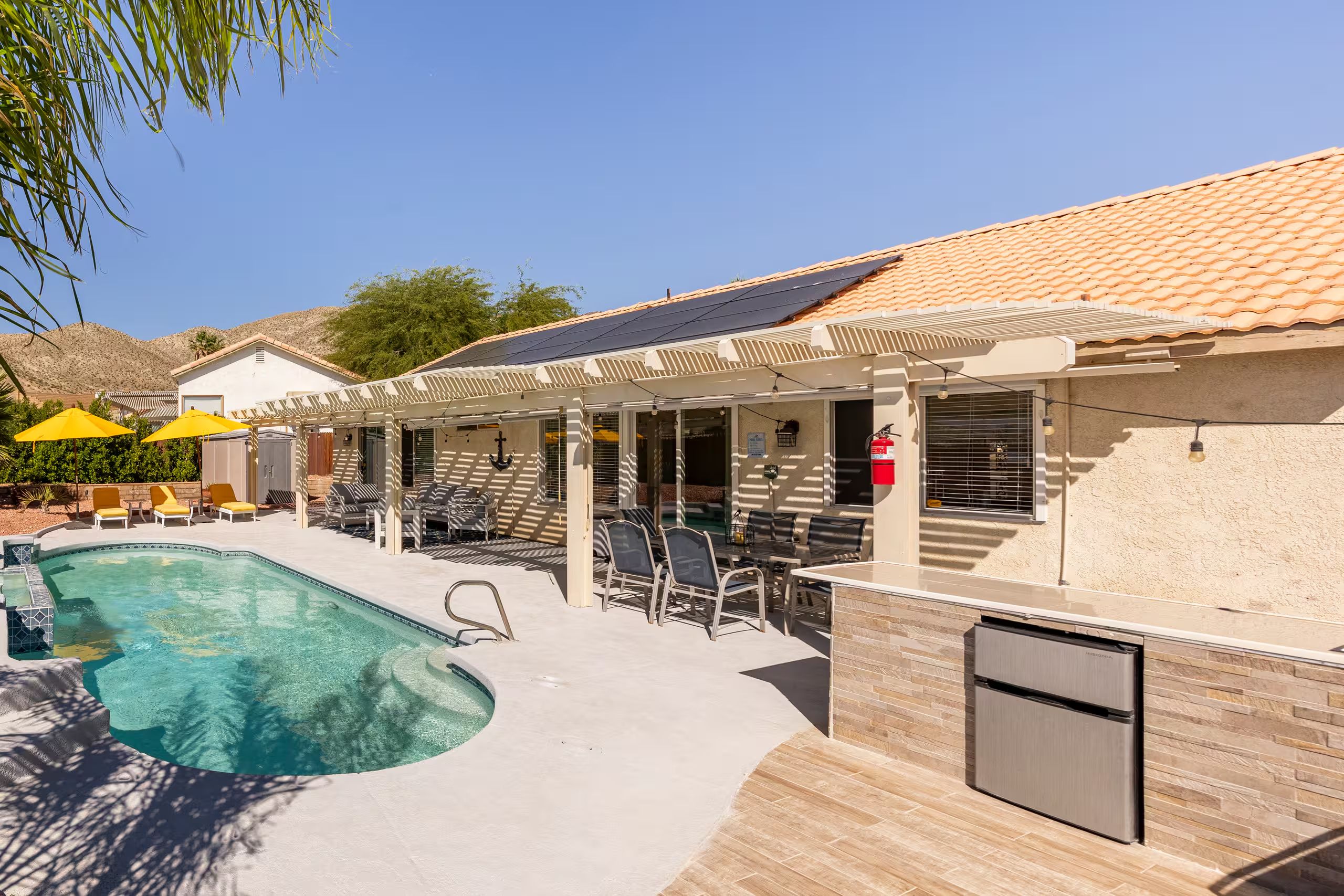 A pool area with a covered seating area, a refrigerator, and a solar panel on the roof.