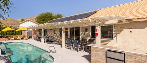 A pool area with a covered seating area, a refrigerator, and a solar panel on the roof.