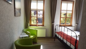 A room with a bed, two green chairs, a radiator, and two windows with curtains. - Double room 2 - Pension Harzer Winkel (Bad Sachsa)