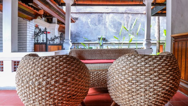 A traditional room with woven rattan chairs, a red bench, and a view of a water body through a window. - OYO 2548 Rasa Sayang Inn (Nusa Dua)