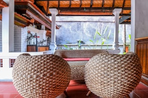 A traditional room with woven rattan chairs, a red bench, and a view of a water body through a window.