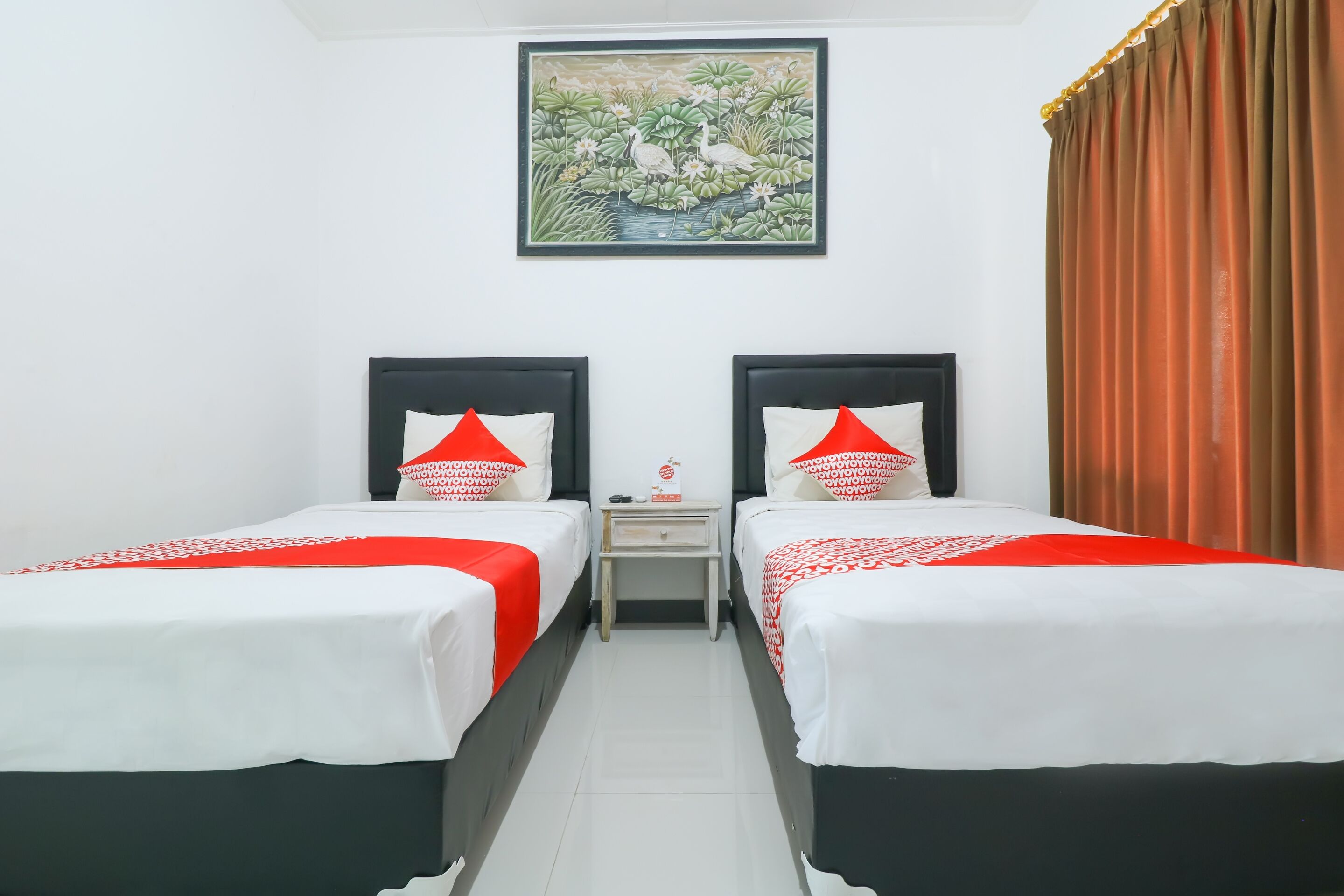 A hotel room with two beds, each with a red and white bedspread, a nightstand, and a painting of a pond with birds on the wall.