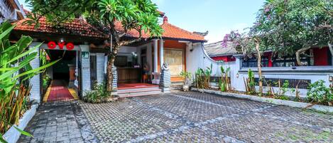 A courtyard with a tiled pathway leading to a building with a red roof and white walls.