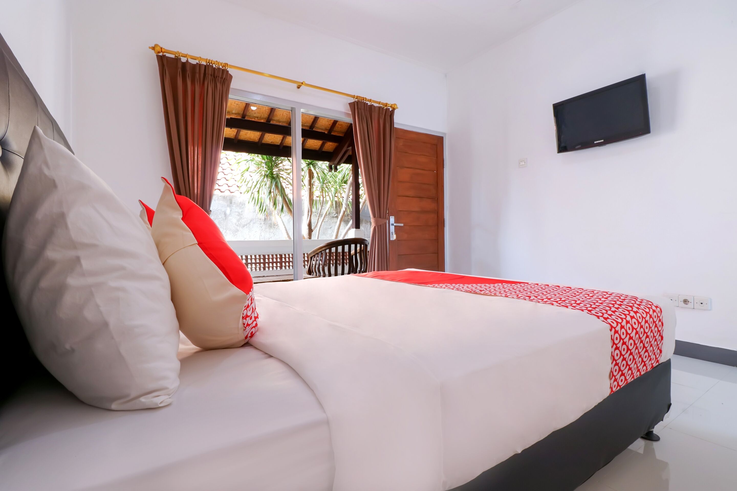 A bedroom with a bed, a TV mounted on the wall, and a window with curtains.