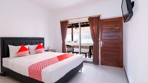 A hotel room with a bed, a TV, a balcony with a table and chairs, and a wooden door. - OYO 2548 Rasa Sayang Inn (Nusa Dua)