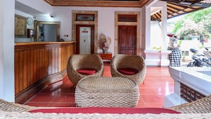 A reception area with a wooden counter, two wicker chairs with red cushions, and a tiled floor. - OYO 2548 Rasa Sayang Inn (Nusa Dua)