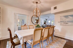 A dining area with a table set for six, a chandelier, and a view of the outdoors. - The Periwinkle House – Bask Poolside at this Sunlit West Palm Retreat (West Palm Beach)